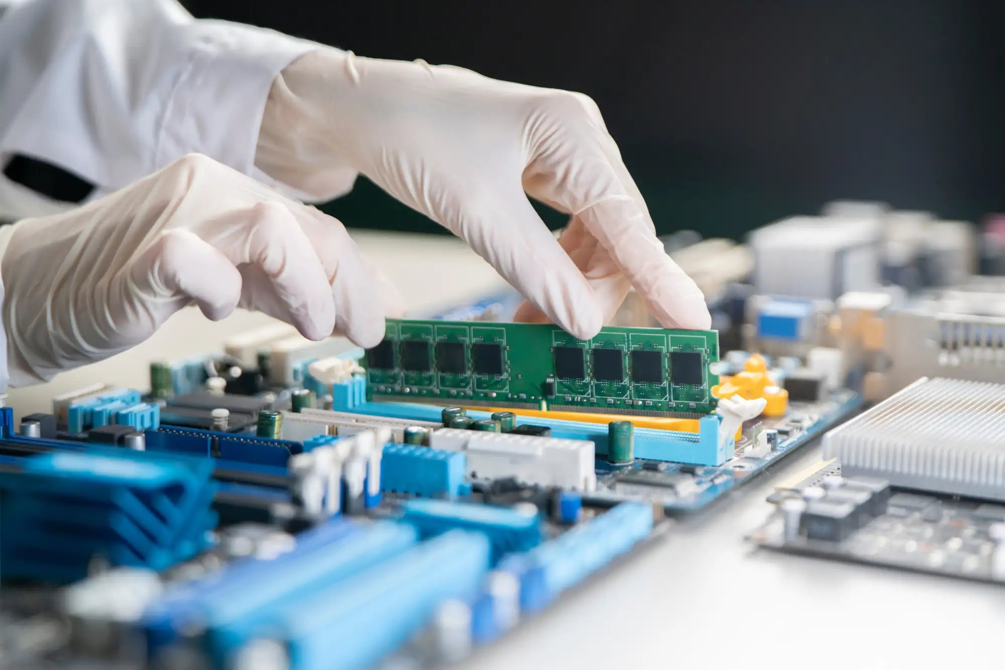 Green ram module with black chips and gold contacts, being handled by gloved hands.